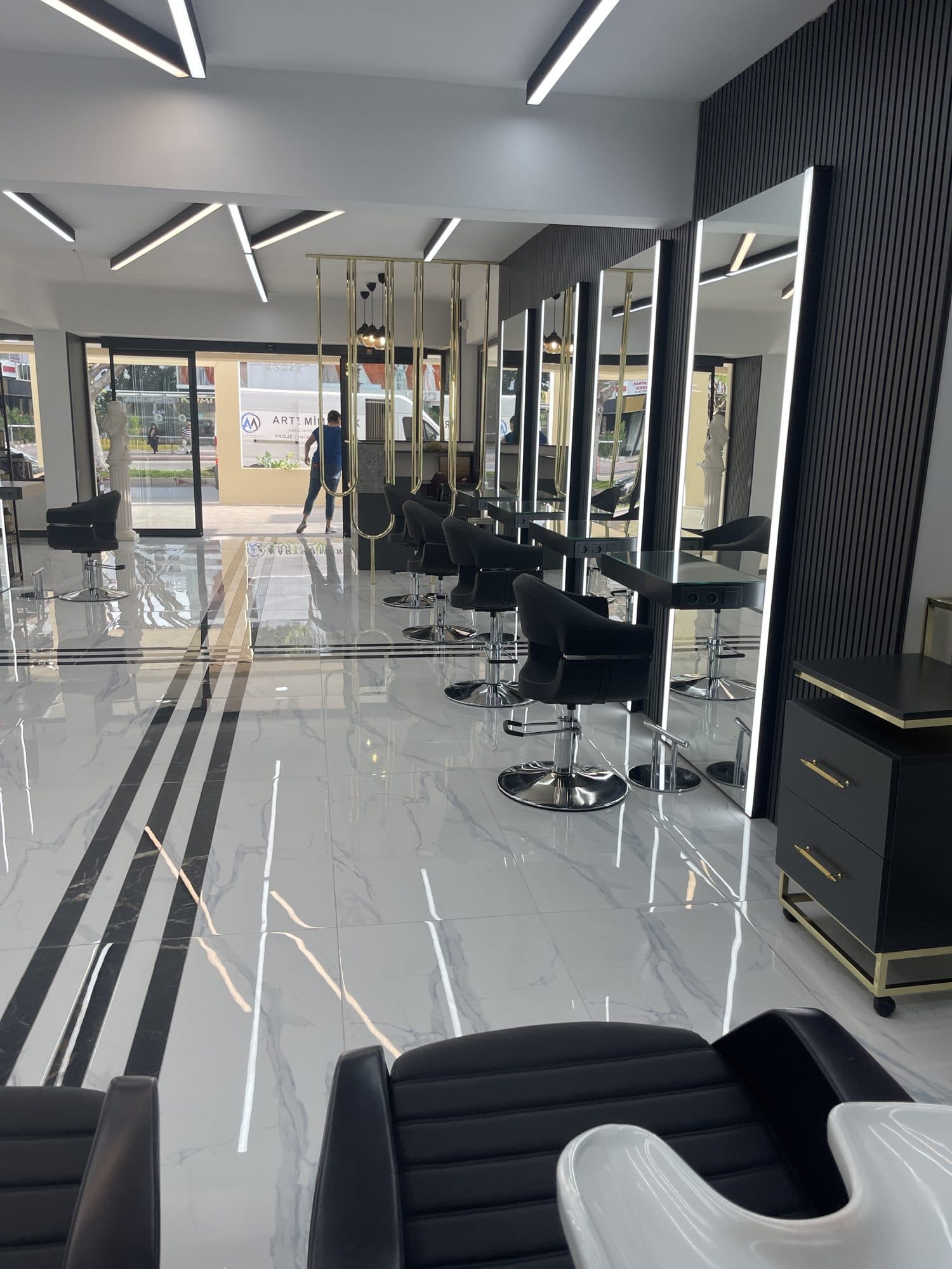 Siyah ve altın detaylı istasyonlara sahip, beyaz mermer zeminli bir kuaför salonu