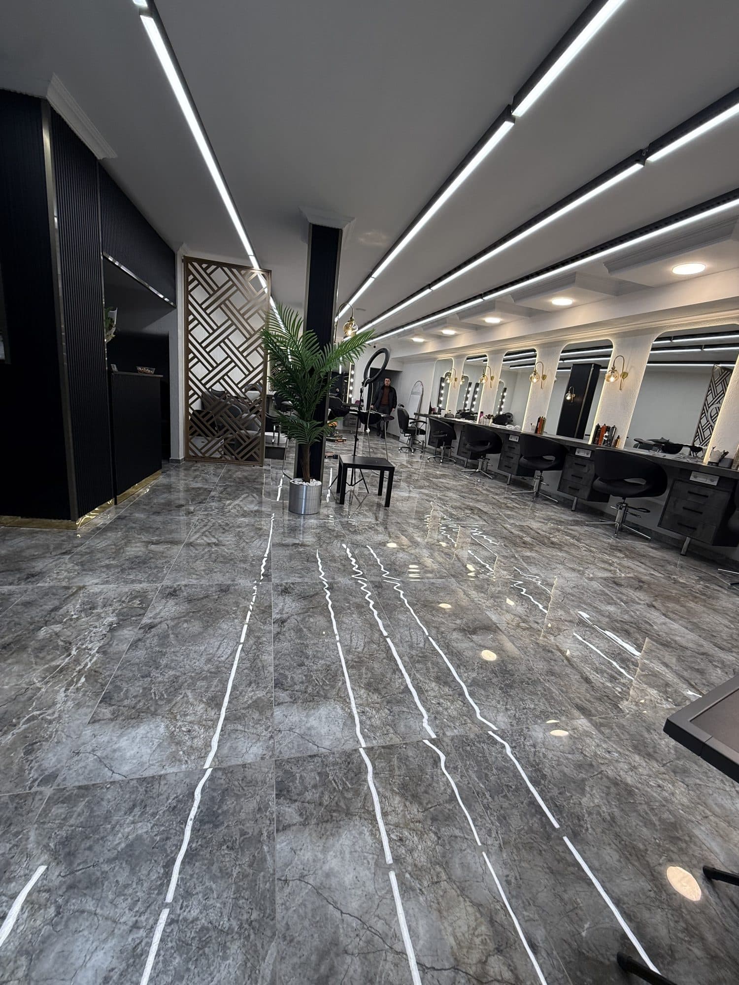 Gri mermer zeminli, siyah kolonlu ve bitki detaylı geniş bir kuaför salonu