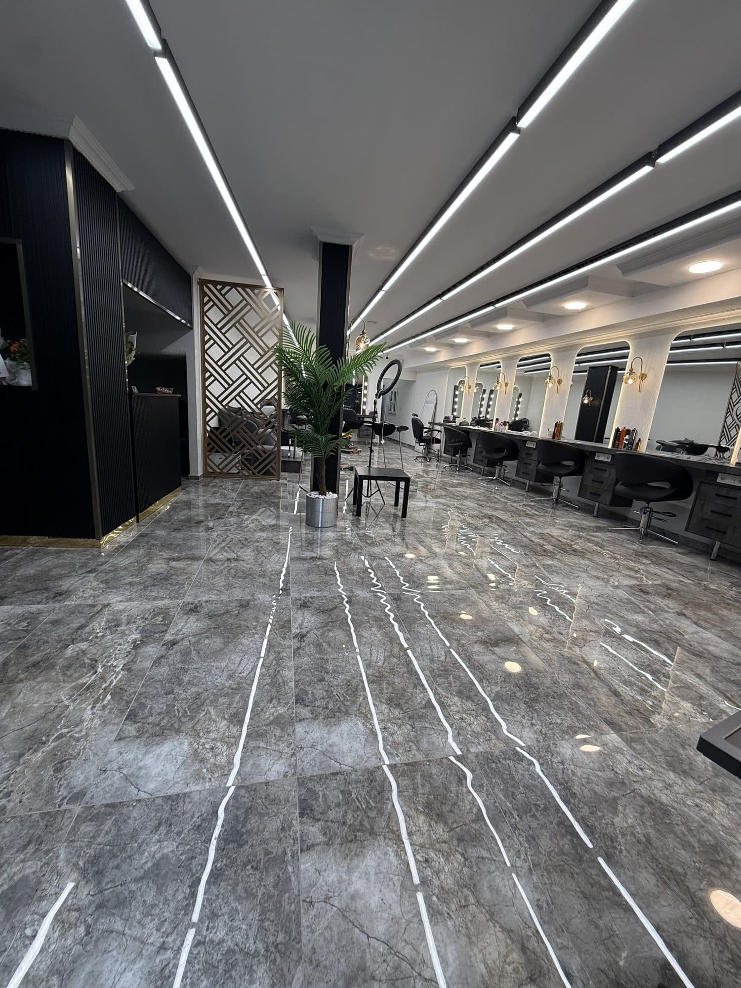 Lineer LED tavan aydınlatmalı ve gri mermer zeminli uzun bir kuaför salonu